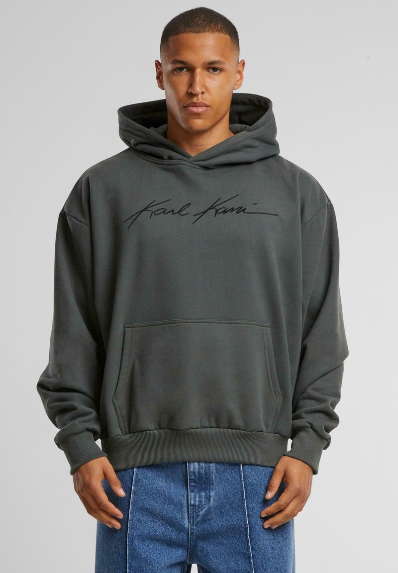 Sudadera gris oscuro con un bolsillo frontal y puños acanalados. Presenta una firma en negro en el pecho. Fabricada con tela suave y con un ajuste relajado.