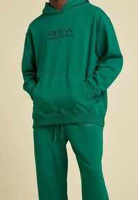 Groene katoenen hoodie met verdiept "GUESS ORIGINALS" logo, kangoeroezak, geribde manchetten en bijpassende joggingbroek met trekkoord.