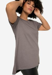 T-shirt gris à manches courtes en tissu léger, offrant une coupe décontractée et des fentes sur les côtés pour faciliter les mouvements. Texture douce et design simple.