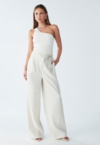 Eno-rameni rebrasti beli top z širokimi, visokim pasom svetlo sivo hlače z vezi na pasu. Gladek, mehak material z nabrano zasnovo.