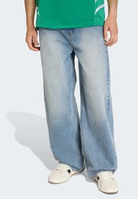 Ljusblå jeans med vida ben i denim, med en blekt utséende. Kombinerade med vita sneakers med svarta detaljer på sidorna.