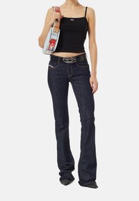 Top ajustado negro, jeans acampanados azul oscuro con costuras en contraste, cinturón negro con hebilla plateada y un bolso de hombro multicolor.