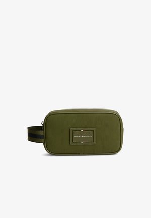 Prostokątna, oliwkowo-zielona kosmetyczka z czarno-pasiastą rączką i naszywką z logo Tommy Hilfiger z przodu.