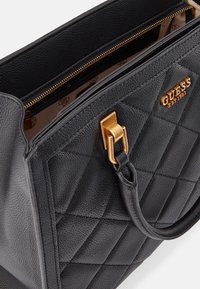 Sac à main en cuir noir texturé avec un design matelassé, ferrures dorées, fermeture éclair supérieure et intérieur avec doublure à motif.