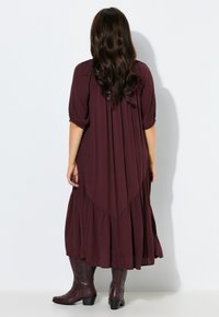 Bordeaux vloeiende maxi-jurk met korte pofmouwen, gelaagde zoom en gemêleerde stof. Gestyled met donkerbruine kniehoge laarzen.