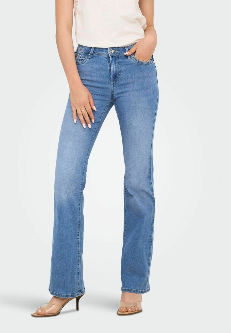 Jeans in denim azzurro chiaro con design a gamba svasata, dotati di tasche frontali e vita media, abbinati a sandali con tacco a stiletto trasparenti.