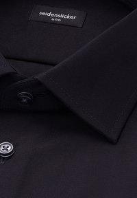 Zwart overhemd met kraag, gemaakt van gladde stof, voorzien van een genaaid label, een sluiting met twee knopen en nauwkeurige stiksels langs de kraag en knopen.