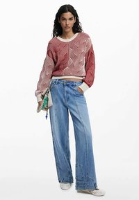 Punaste ja valgete triipudega kudumispusa lahtiste varrukatega, kombineeritud siniste laia säärega teksapükstega. Aksessuaar: väike beež käekott võtmehoidjaga.