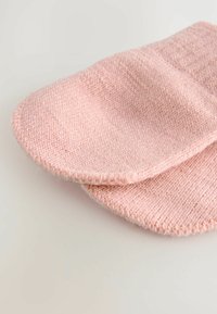 Des moufles tricotées rose pâle sont posées à plat sur un fond clair, mettant en valeur leur texture et leurs bords arrondis.