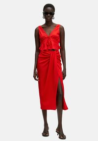 Rode two-piece jurk met een gestructureerde cropped top met een volant en een hoge split, wikkelstijl rok. Geaccentueerd met stijlvolle zwarte sandalen.