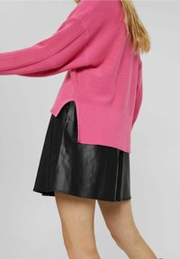 Różowy sweter wełniany z ribbowanym dołem i bocznymi rozporkami, w połączeniu z krótką czarną skórzaną spódnicą. Miękka faktura i luźny krój.