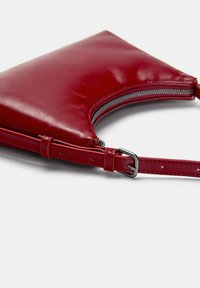 Red leather handbag with a curved design, featuring a zip closure and adjustable strap. Smooth texture, minimal hardware, and functional details.