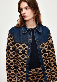 Jeansjacka med mönstrade ärmar i brunt och marinblått, med knappstängning, krage och kontrasterande texturer.