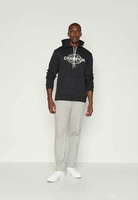 Felpa nera con logo "CHAMPION" sul davanti, abbinata a pantaloni della tuta grigio chiaro e sneakers bianche. Design semplice, vestibilità casual.