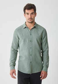 Green linen button-up shirt with long sleeves, raised collar, and matching buttons. Features a textured, slightly translucent fabric.