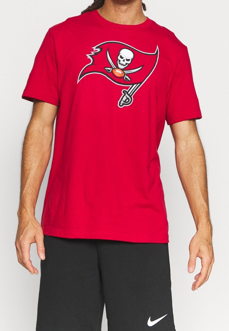 Homme portant un t-shirt rouge avec un logo de drapeau pirate tenant un ballon de football et un short noir Nike.
