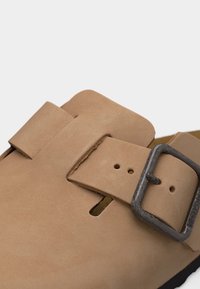 Ταμπά δερμάτινο σανδάλι με κούμπωμα από μέταλλο και ρυθμιζόμενο λουρί, που δείχνει λεπτομερή ραφή και υφή υλικού.