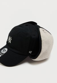 Casquette noire avec logo brodé blanc, équipée de rabats d'oreilles en fourrure. Fabriquée en coton, avec une visière incurvée et une sangle arrière ajustable.