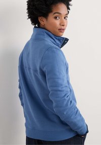 Giacca in fleece blu con colletto alto e zip, caratterizzata da maniche lunghe e un design a cucitura piatta. Texture morbida e vestibilità casual.