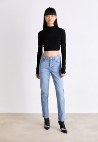 Svart kortärmad topp med lång ärm i kombination med högmidjade ljusblå jeans med fem knappar fram. Modellen bär svarta spetsiga ankla stövlar.