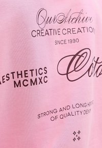 Helehele roosa puuvillane T-särk, millel on musta teksti erinevates fontides ja graafikatega, sealhulgas "Creative Creations" ja "Strong and Long Heritage".