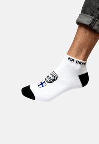 Calcetín blanco de tobillo con acentos en negro. Presenta un gráfico de un hombre con barba y una bandera finlandesa. Texto "MR UKKO" cerca del puño.