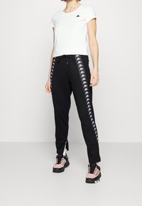 Svarta sweatpants med vita sidostreck och en logotyp, tillsammans med en vit kortärmad T-shirt. Inkluderar även rosa och svarta sneakers.