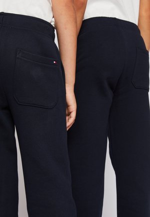 Granatowe spodnie dresowe o gładkiej fakturze, z kieszenią po każdej stronie i małym logo przy tylnej kieszeni.