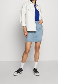 Bílá oversized košile s jaketovým stylem a zlatými knoflíky, modré tričko, světle modrá džínsová minisukně a černé tenisky s bílou podrážkou.