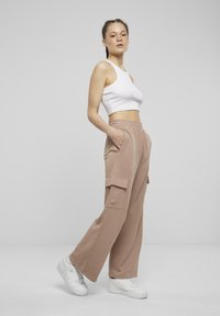 Ljust beige cargobyxor i mjukt material, med resår i midjan och flera fickor, kombinerat med en vit croptop och vita sneakers.