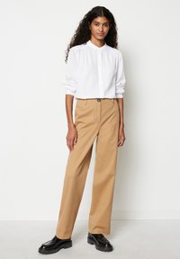 White button-up shirt with a high collar, paired with light brown wide-leg trousers and black chunky shoes. Smooth fabric, tailored fit.
