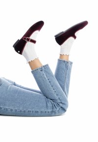 Zapatos Mary Jane de terciopelo burdeos con hebilla, usados con calcetines blancos de canalé, combinados con jeans de mezclilla azul claro, piernas levantadas.