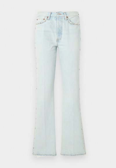 Jean en denim bleu clair taille haute avec jambes évasées, poches avant et arrière, fermeture par bouton et zip, et clous étoiles en métal le long des coutures extérieures.
