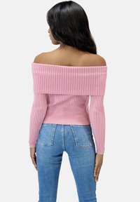 Rosa gerippter Off-Shoulder-Pullover mit langen Ärmeln, ausgestattet mit einem breiten, gerippten Halsausschnitt und tailliertem Schnitt, kombiniert mit hellen Jeans.