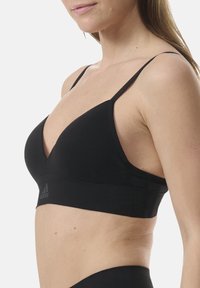 Svart triangel-bh med tunna justerbara remmar, tillverkad av en slät tyg, med ett brett band nederst med subtil logotyp.