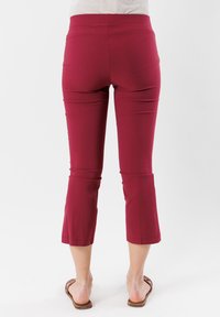 Pantaloni capri bordeaux realizzati in tessuto elasticizzato, con vita alta e lunghezza alla caviglia, caratterizzati da una texture liscia e senza motivi visibili.