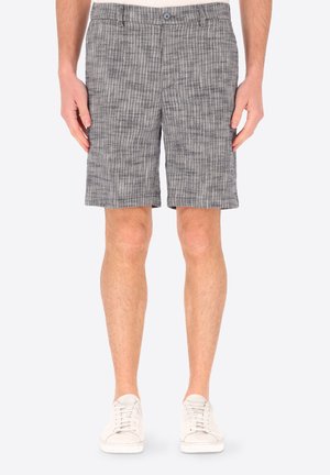 Uomo che indossa pantaloncini grigi testurizzati fino al ginocchio e sneakers bianche, in piedi con le braccia rilassate lungo i fianchi su sfondo bianco.