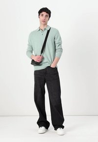 Světl zelený polo svetr, volné černé džíny a bílé tenisky. Modelka nese malou černou crossbody tašku. Hladká textura, ležérní střih.