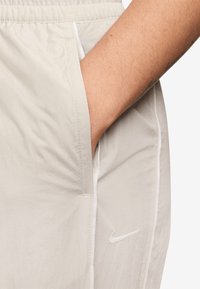 Gaišpelēku sporta šorti, kas izgatavoti no viegla auduma, ar sānu kabatu un baltu Nike logo priekšā. Gluda tekstūra, elastīgs jostasvieds.
