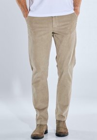 Beige Cordura-Hosen mit geradem Schnitt, ausgestattet mit Seitentaschen und einer subtilen Rippstruktur. Getragen mit braunen Wildlederstiefeln.