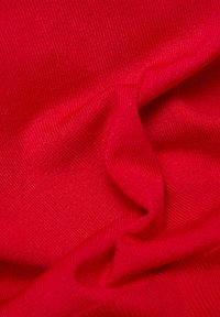 Roter Strickstoff mit feiner, strukturierter Webart, der Falten und Knicke aufweist und so seine Weichheit und Flexibilität betont.