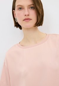 Top rosa chiaro a maniche corte con scollo rotondo, texture liscia e vestibilità morbida. Presenta un collo a costine e dettagli di cucitura discreti.