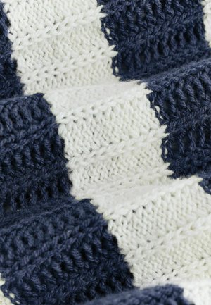 Közelkép puha kötött anyagról, váltakozó sötétkék és fehér cikk-cakk mintával és texturált öltésekkel.