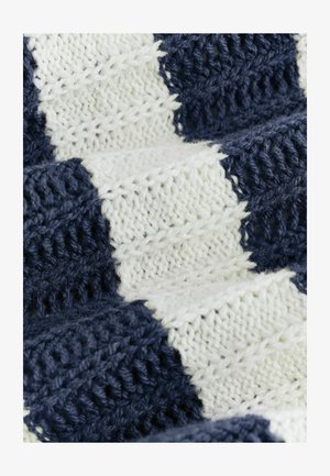 Közelkép puha kötött anyagról, váltakozó sötétkék és fehér cikk-cakk mintával és texturált öltésekkel.