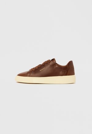 Brown leather sneaker with round toe, textured surface, and contrasting cream rubber sole. Features tonal lace-up design and branding.