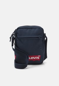 Borsa a spalla in nylon blu navy con tracolla regolabile, tasche con zip e logo rosso Levi's ben visibile davanti. Forma rettangolare compatta.