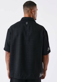 Zwarte short-sleeve shirt met een gestructureerd patroon, een kraag en merkaccenten op de mouwen en de achterkant. Casual pasvorm.
