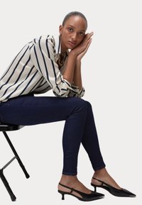 Svarta slingback-hälar med spetsiga tår, bärs med mörka denimjeans och en vit skjorta med marinblå ränder. Slät textur, skräddarsydd passform.