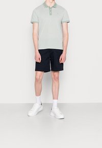 Polo shirt vert clair avec col, associé à un short marine. Des baskets blanches et des chaussettes de cur completent la tenue. Design simple, coupe décontractée.