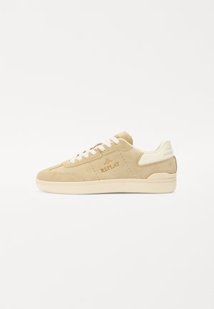 Beige suède sneakers met een laag bovenwerk, voorzien van witte veters, een geperst logo en een rubberen zool met textuur. Accenten omvatten perforaties.